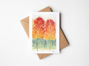 Watercolour greeting card featuring a vibrant autumn forest with rich reds, oranges, and yellows. The design captures the warmth and beauty of the fall season.