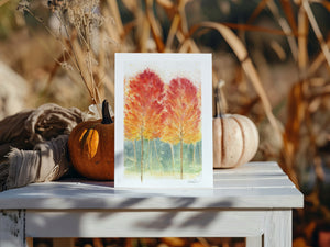 Watercolour greeting card featuring a vibrant autumn forest with rich reds, oranges, and yellows. The design captures the warmth and beauty of the fall season.