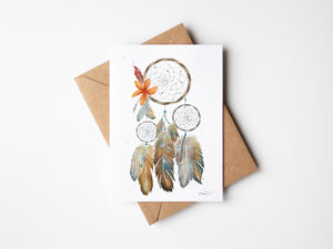 Watercolour greeting card featuring a dreamcatcher with vibrant orange and crimson feathers. The design symbolizes healing, reconciliation, and remembrance, reflecting the connection between tradition and the earth.