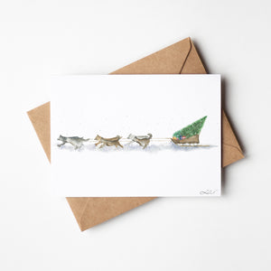 Santa’s Sled Dogs Greeting Card – Eco-friendly greeting card featuring a whimsical watercolour illustration of Santa’s Sled Dogs delivering a Christmas tree, bringing holiday cheer.