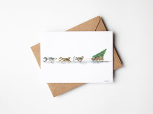 Santa’s Sled Dogs Greeting Card – Eco-friendly greeting card featuring a whimsical watercolour illustration of Santa’s Sled Dogs delivering a Christmas tree, bringing holiday cheer.