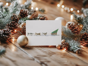 Santa’s Sled Dogs Greeting Card – Eco-friendly greeting card featuring a whimsical watercolour illustration of Santa’s Sled Dogs delivering a Christmas tree, bringing holiday cheer.