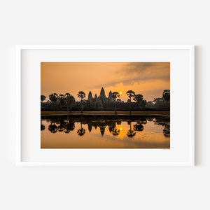 Fine art landscape photograph of Angkor Wat at sunrise, with golden light, sun mirrored in still water, and a serene, atmospheric temple silhouette.