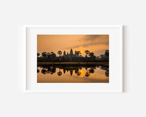 Fine art landscape photograph of Angkor Wat at sunrise, with golden light, sun mirrored in still water, and a serene, atmospheric temple silhouette.