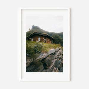 Dreamy hidden wooden cabin beneath a mountain in Norway, moody fine art landscape photography print.