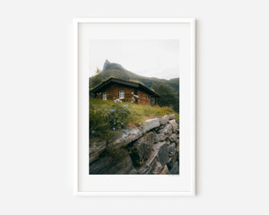 Dreamy hidden wooden cabin beneath a mountain in Norway, moody fine art landscape photography print.