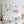Three framed hand-painted watercolour art prints of Paris landmarks—the Eiffel Tower, Sacré-Cœur and Versailles Palace—displayed above a white sofa on a bright, elegant panelled wall.