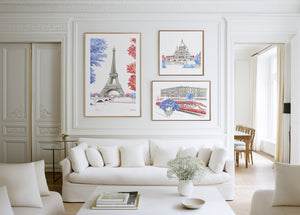 Three framed hand-painted watercolour art prints of Paris landmarks—the Eiffel Tower, Sacré-Cœur and Versailles Palace—displayed above a white sofa on a bright, elegant panelled wall.