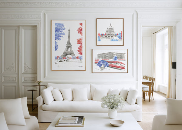 Three framed hand-painted watercolour art prints of Paris landmarks—the Eiffel Tower, Sacré-Cœur and Versailles Palace—displayed above a white sofa on a bright, elegant panelled wall.