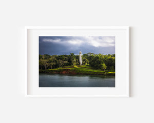 White lighthouse standing along the Panama Canal, captured in a minimal fine art photograph emphasizing calm water and quiet light.