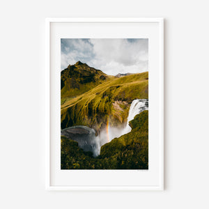 Vertical fine art photograph of Skógafoss waterfall in Iceland with mist and a faint rainbow in the spray.