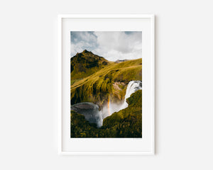 Vertical fine art photograph of Skógafoss waterfall in Iceland with mist and a faint rainbow in the spray.