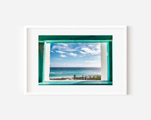 Fine art photograph of the ocean through a lighthouse window with a post and signs, exploring light, texture, and a sense of calm reflection.