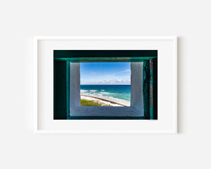 View of turquoise ocean through a lighthouse window, showcasing calm coastal scenery with light and texture in a fine art photograph.
